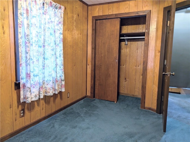 unfurnished bedroom with dark carpet, wooden walls, and a closet