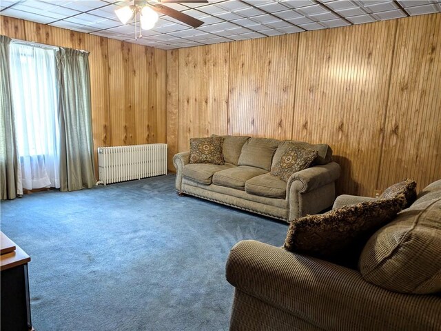 living room featuring ceiling fan, radiator, wood walls, and carpet flooring