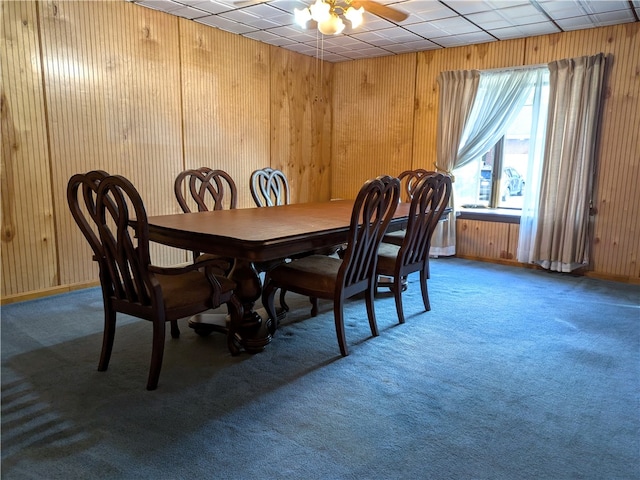 dining area with carpet, a drop ceiling, wood walls, and ceiling fan