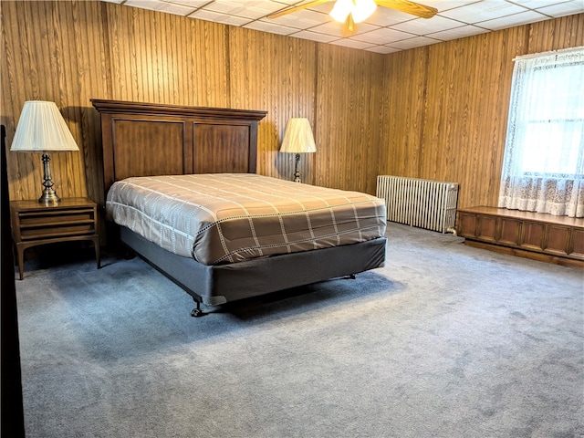 bedroom featuring wooden walls, carpet, radiator, and ceiling fan