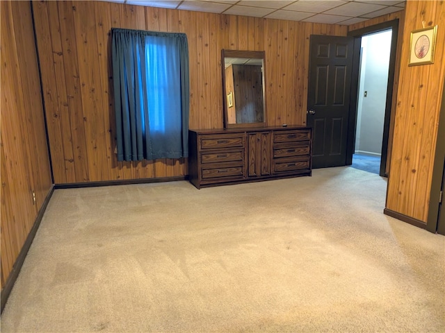 unfurnished bedroom with a drop ceiling, wooden walls, and light colored carpet