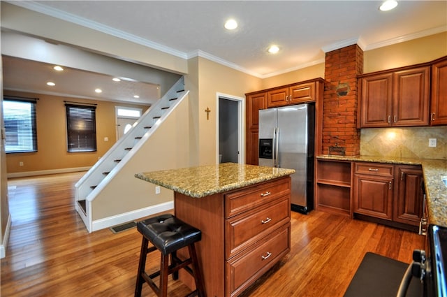 kitchen featuring ornamental molding, wood-type flooring, stainless steel refrigerator with ice dispenser, and a kitchen island