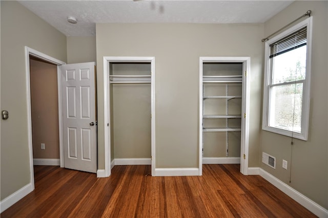 unfurnished bedroom featuring a textured ceiling, two closets, and dark wood-type flooring