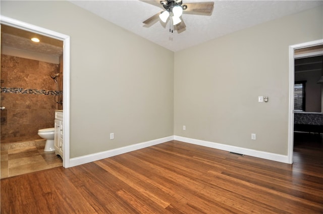 unfurnished bedroom with wood-type flooring, a textured ceiling, connected bathroom, and ceiling fan