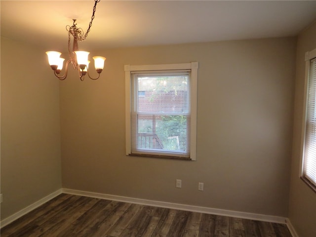 spare room featuring an inviting chandelier and dark hardwood / wood-style flooring