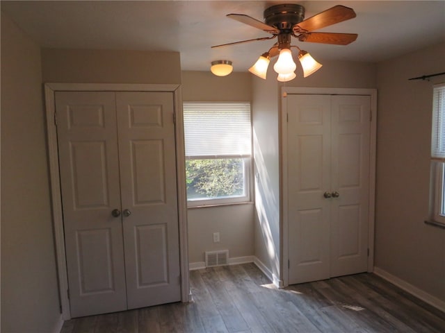 unfurnished bedroom with ceiling fan, two closets, and dark hardwood / wood-style flooring