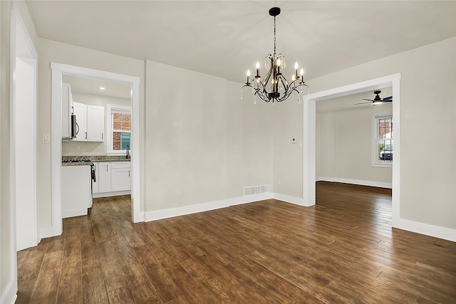 empty room featuring ceiling fan with notable chandelier and dark hardwood / wood-style flooring