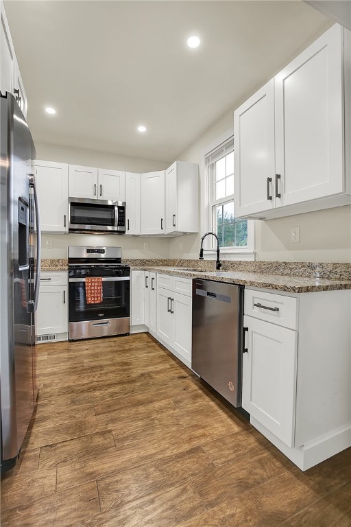 kitchen with dark wood-type flooring, sink, white cabinets, stainless steel appliances, and light stone countertops