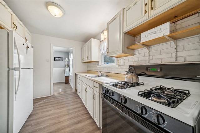 kitchen with decorative backsplash, light hardwood / wood-style floors, black range with gas stovetop, white fridge, and sink