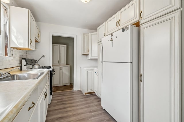 kitchen with light wood-type flooring, white refrigerator, sink, white cabinets, and stainless steel stove