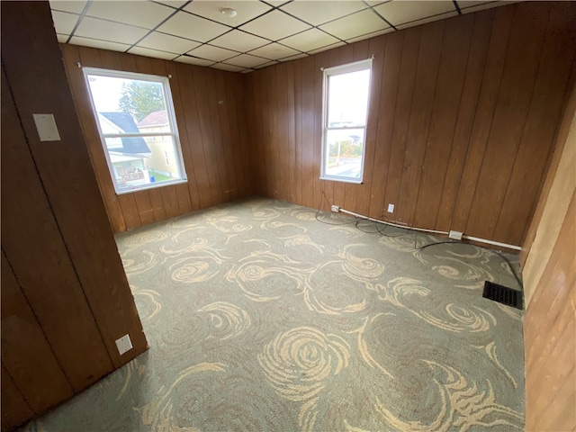 carpeted empty room featuring wooden walls and a paneled ceiling