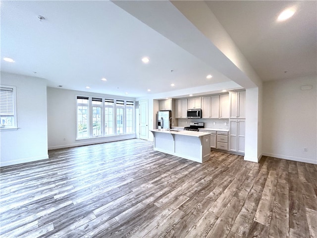 kitchen with an island with sink, sink, wood-type flooring, gray cabinets, and appliances with stainless steel finishes