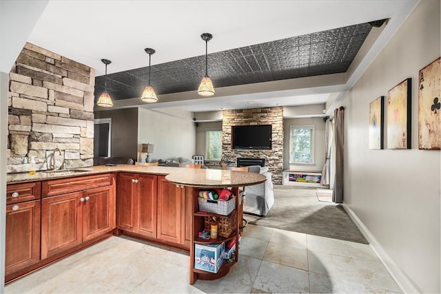 kitchen with pendant lighting, light stone countertops, sink, light colored carpet, and a fireplace