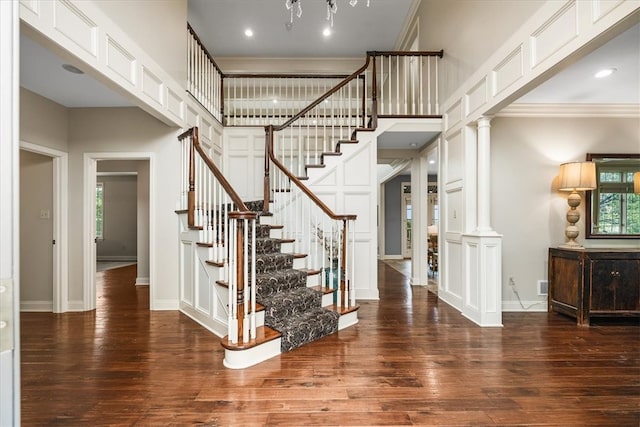 staircase with ornamental molding, wood-type flooring, a towering ceiling, and decorative columns