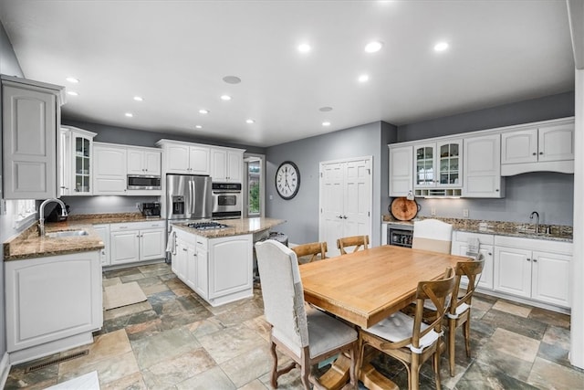 kitchen with white cabinetry, a kitchen island, stainless steel appliances, dark stone counters, and sink