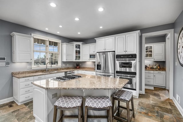 kitchen with appliances with stainless steel finishes, a kitchen island, sink, and white cabinets