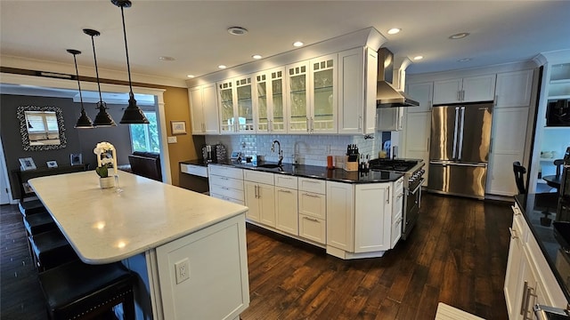 kitchen featuring a center island, dark hardwood / wood-style floors, wall chimney range hood, appliances with stainless steel finishes, and decorative light fixtures