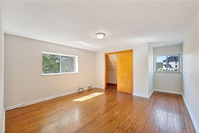 unfurnished bedroom featuring hardwood / wood-style flooring, a closet, multiple windows, and a spacious closet