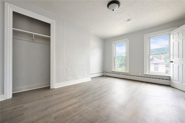 unfurnished bedroom with hardwood / wood-style flooring, baseboard heating, and a closet