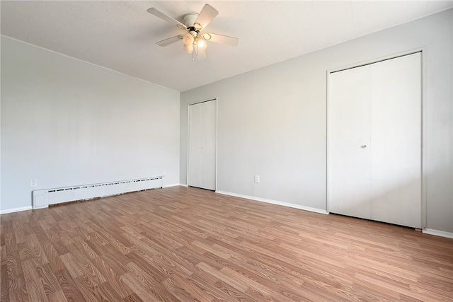 interior space with ceiling fan, multiple closets, baseboard heating, and light wood-type flooring