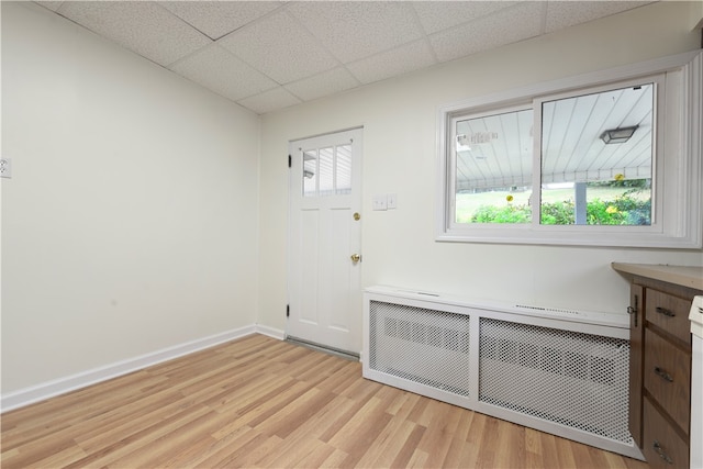 unfurnished room featuring light hardwood / wood-style flooring, radiator, a healthy amount of sunlight, and a paneled ceiling