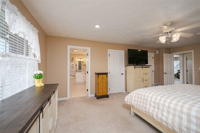 bedroom with ceiling fan, light colored carpet, and ensuite bathroom