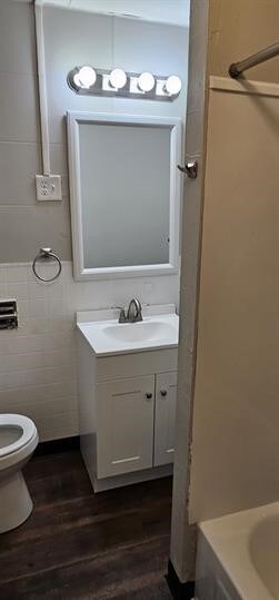 bathroom featuring wood-type flooring, tile walls, vanity, and toilet