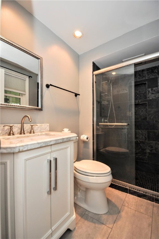 bathroom featuring vanity, a shower with shower door, toilet, and tile patterned floors