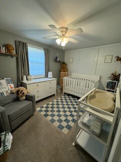 bedroom featuring a crib, dark colored carpet, and ceiling fan