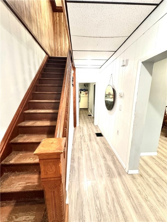 staircase featuring wood-type flooring, a drop ceiling, and wood walls