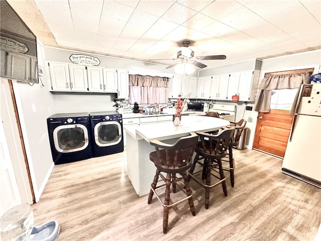 kitchen featuring a breakfast bar, white refrigerator, separate washer and dryer, a center island, and ceiling fan