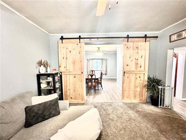 living room featuring a barn door, ornamental molding, hardwood / wood-style floors, and ceiling fan