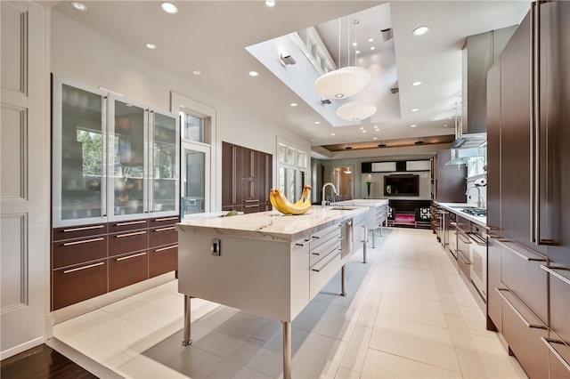 kitchen with a large island, pendant lighting, light stone counters, sink, and high end fridge