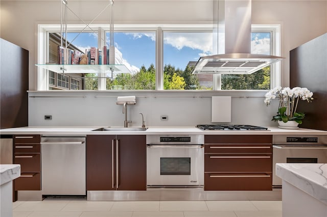 kitchen with appliances with stainless steel finishes, light stone counters, island range hood, dark brown cabinets, and sink