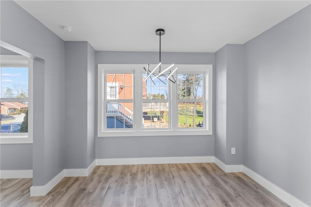 unfurnished dining area with an inviting chandelier, plenty of natural light, and light hardwood / wood-style flooring