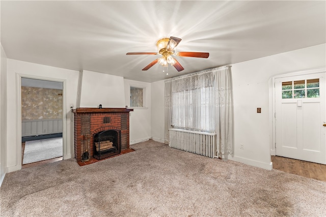 unfurnished living room featuring carpet flooring, radiator, ceiling fan, and a brick fireplace