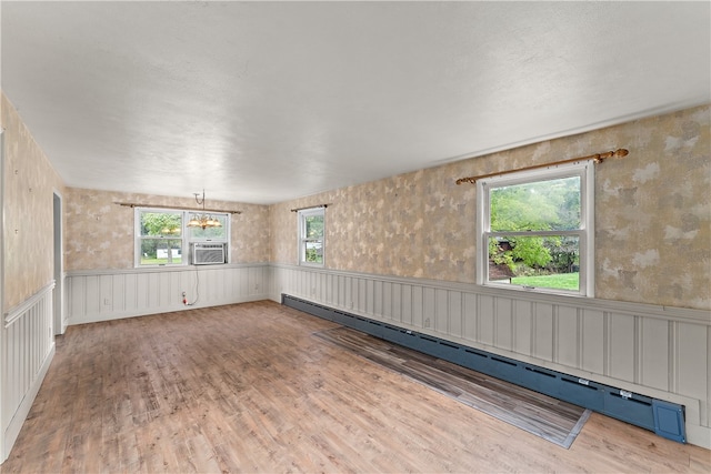 empty room featuring a baseboard radiator, light hardwood / wood-style flooring, a notable chandelier, and a healthy amount of sunlight