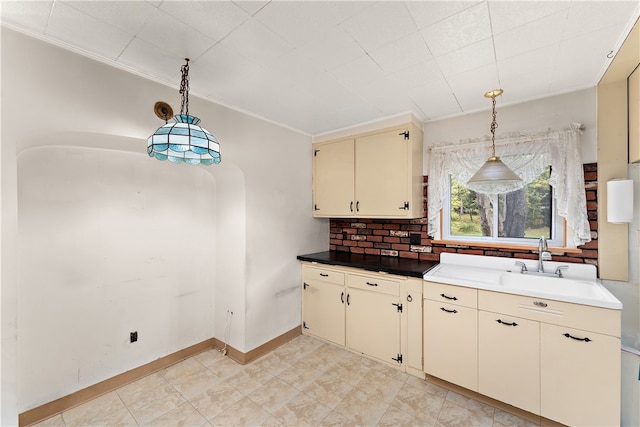 kitchen with crown molding, backsplash, cream cabinets, and pendant lighting