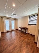 interior space with a drop ceiling, french doors, and dark hardwood / wood-style flooring