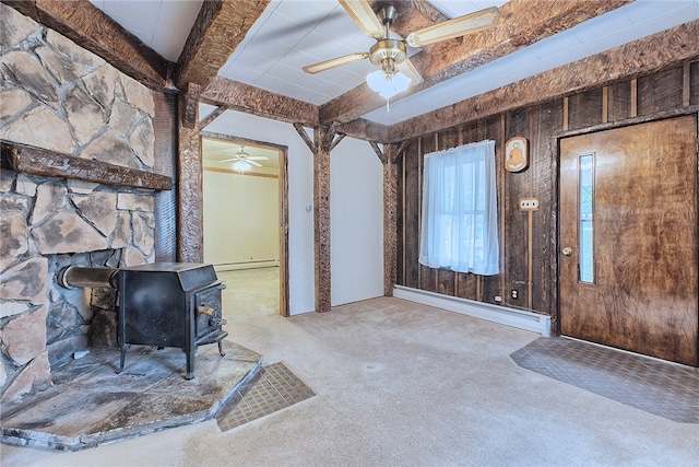 interior space with a wood stove, wood walls, light colored carpet, a baseboard radiator, and ceiling fan