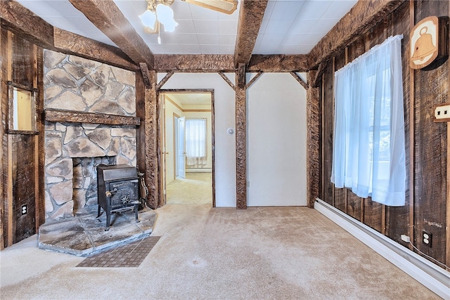 unfurnished living room with carpet floors, beam ceiling, ceiling fan, and a wood stove