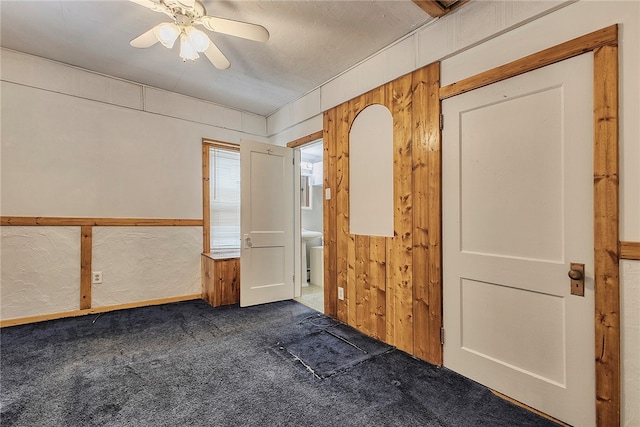 unfurnished bedroom featuring wooden walls, dark colored carpet, and ceiling fan