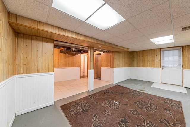 finished basement featuring visible vents, a drop ceiling, and wooden walls
