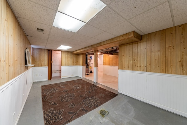 basement featuring water heater, wooden walls, and a paneled ceiling