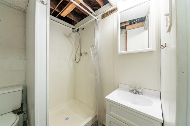 full bathroom featuring concrete block wall, toilet, vanity, and a shower stall
