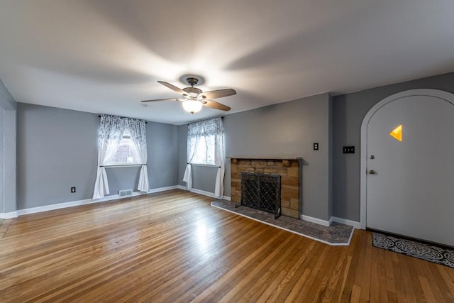 unfurnished living room featuring hardwood / wood-style flooring, baseboards, visible vents, arched walkways, and ceiling fan