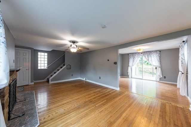 unfurnished living room with light wood finished floors, stairs, a fireplace, and a wealth of natural light