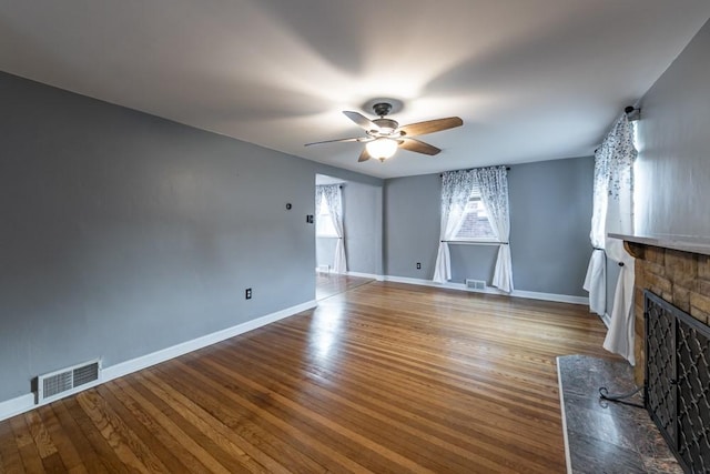 unfurnished living room with ceiling fan, visible vents, wood finished floors, and a stone fireplace