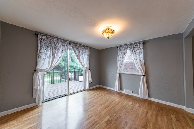 empty room with a textured ceiling and light hardwood / wood-style flooring