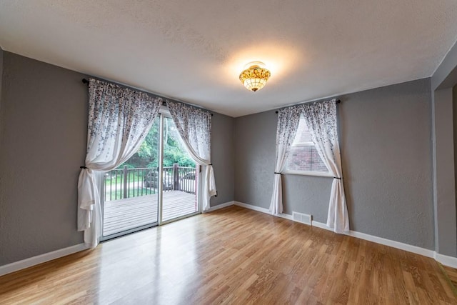 empty room featuring a textured wall, baseboards, a textured ceiling, visible vents, and wood finished floors